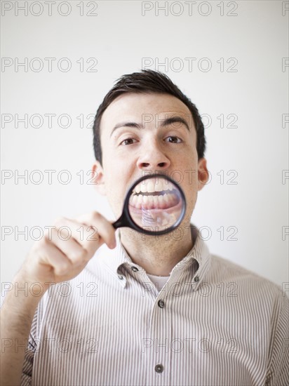 Man looking standing looking through magnifying glass. 
Photo : Jessica Peterson