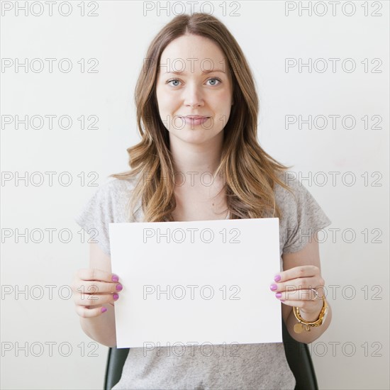 Portrait of cheerful young woman holding blank card. 
Photo : Jessica Peterson