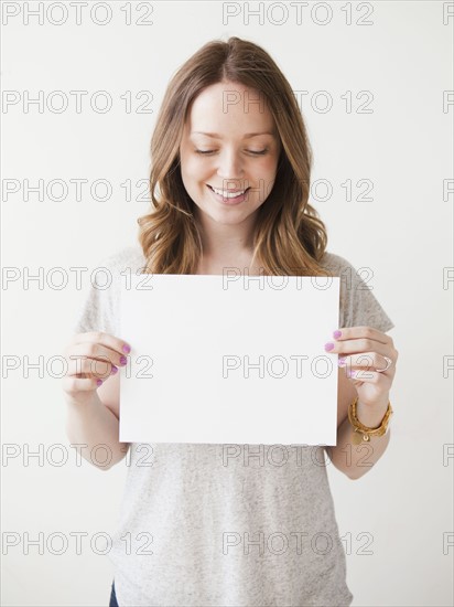 Portrait of cheerful young woman holding blank card. 
Photo : Jessica Peterson