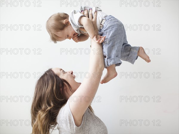 Young mother lifting baby boy (6-11 months) mid-air. 
Photo : Jessica Peterson