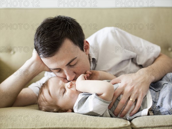 Father and baby boy (6-11 months) lying on sofa. 
Photo : Jessica Peterson