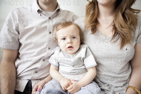 Young couple with baby boy (6-11 months) sitting on sofa. 
Photo : Jessica Peterson