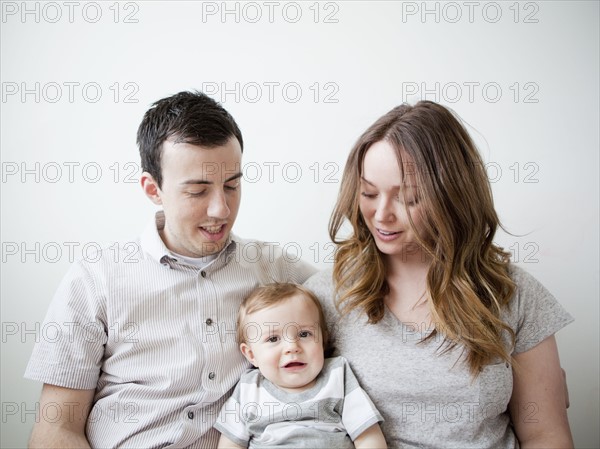 Young couple with baby boy (6-11 months) sitting on sofa. 
Photo : Jessica Peterson