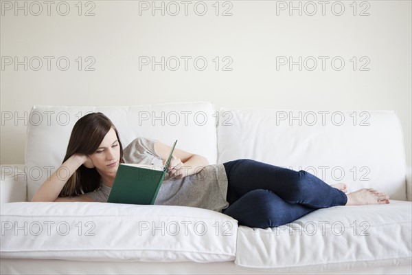 Young woman reclining on bed, reading book. 
Photo: Jessica Peterson