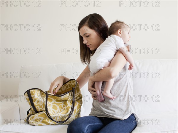 Mother reaching in her handbag white embracing baby girl (2-5 months). 
Photo : Jessica Peterson