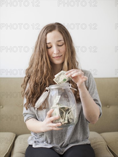 Young woman putting money into her savings jar . 
Photo: Jessica Peterson