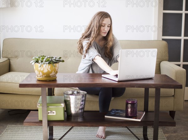 Young attractive woman using laptop while sitting on sofa. 
Photo : Jessica Peterson