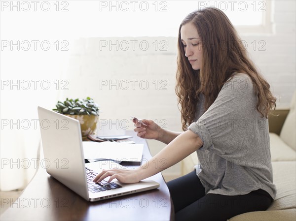 Young attractive woman using laptop while sitting on sofa. 
Photo : Jessica Peterson