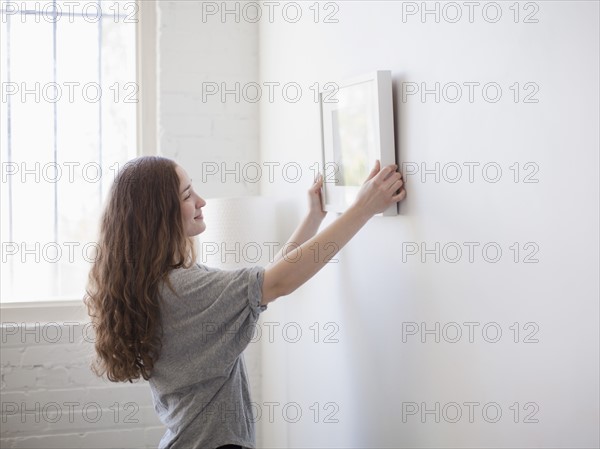 Young woman hanging picture on freshly painted wall. 
Photo: Jessica Peterson