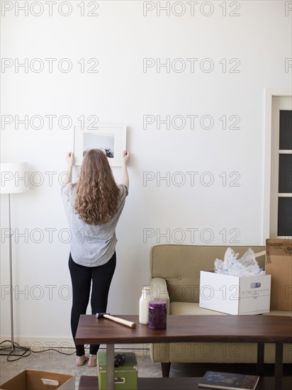 Young woman hanging picture on freshly painted wall. 
Photo : Jessica Peterson