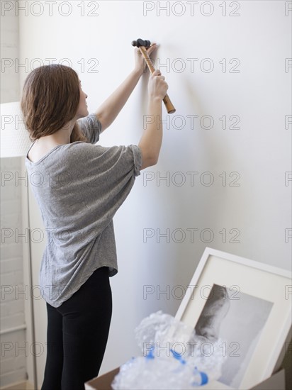 Young woman hanging picture on freshly painted wall. 
Photo : Jessica Peterson