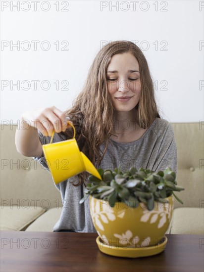 Young woman watering pot plant . 
Photo : Jessica Peterson