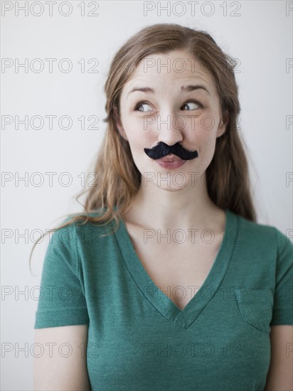 Studio shot of happy young woman with fake moustache. 
Photo : Jessica Peterson