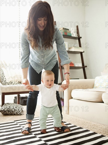 Young mother assisting baby boy (6-11 months) in his first steps. 
Photo : Jessica Peterson