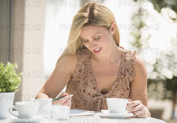 Woman writing journal at outdoor cafe table.