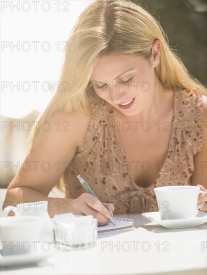 Woman writing journal at outdoor cafe table.