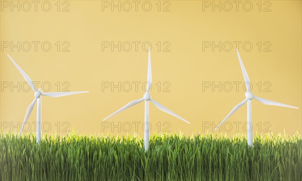 Model wind turbines in grass on yellow background.