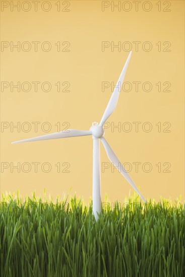 Model wind turbines in grass on yellow background.