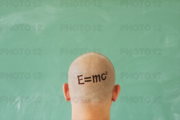 Man with formula on head in front of blackboard.