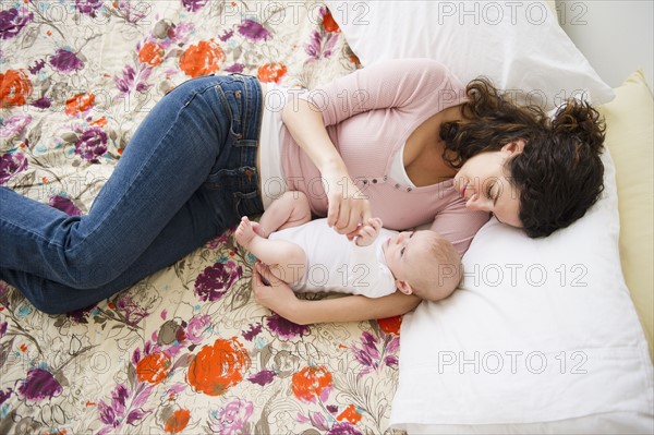 Mother and baby boy (2-5 months) lying together on bed. Photo : Jamie Grill