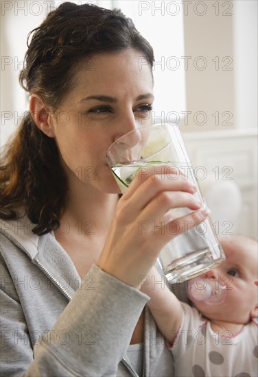 Mother drinking water with baby boy (2-5 months) beside her . Photo : Jamie Grill