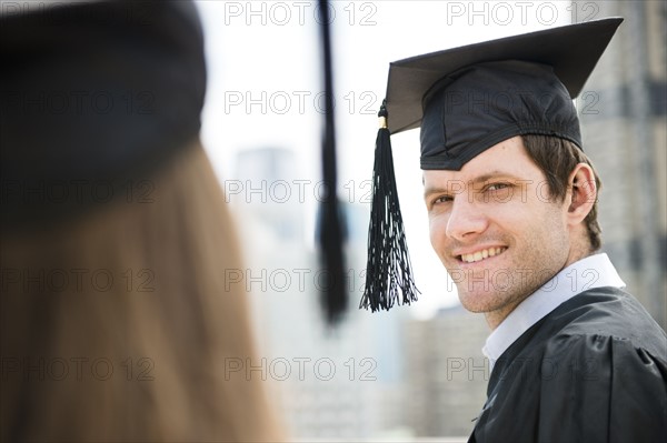 Young man and woman wearing graduation gowns. Photo : Jamie Grill