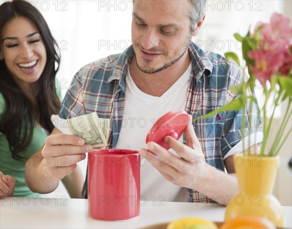 Couple putting money in savings jar. Photo : Jamie Grill