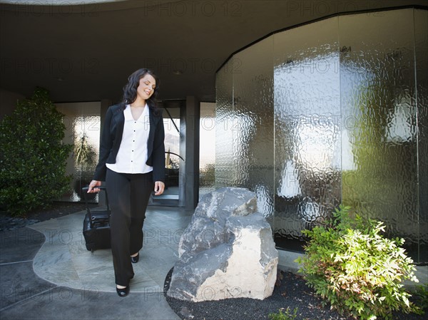 Woman leaving house with piece of luggage.