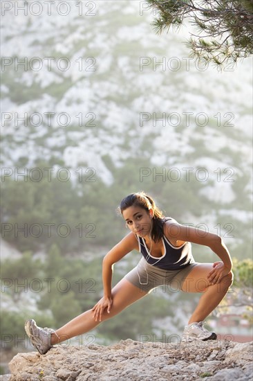 France, Marseille, Young woman stretching on cliff. Photo : Mike Kemp