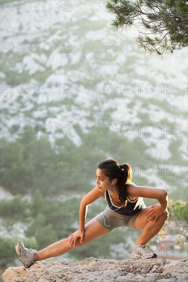 France, Marseille, Young woman stretching on cliff. Photo : Mike Kemp