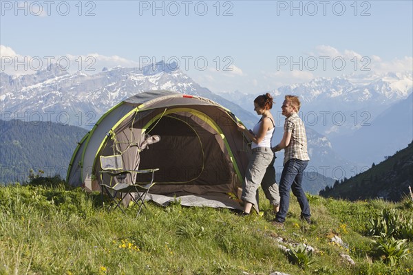 Switzerland, Leysin, Hikers pitching tent on meadow. Photo : Mike Kemp