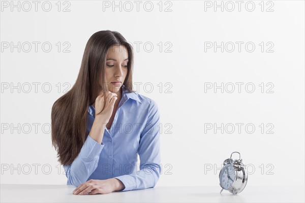 Studio shot of woman looking at alarm clock. Photo : Jan Scherders