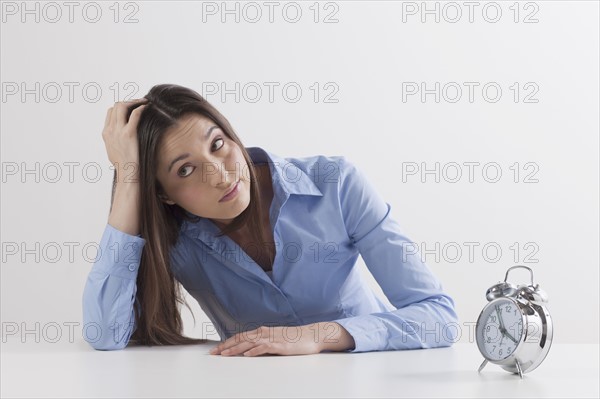 Studio shot of woman waiting by alarm clock. Photo: Jan Scherders