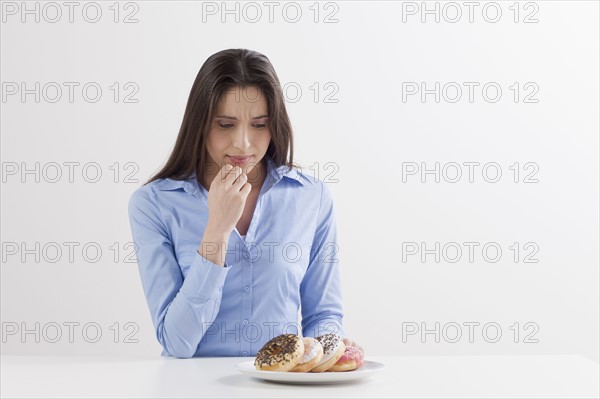 Studio shot of woman looking at donuts. Photo : Jan Scherders