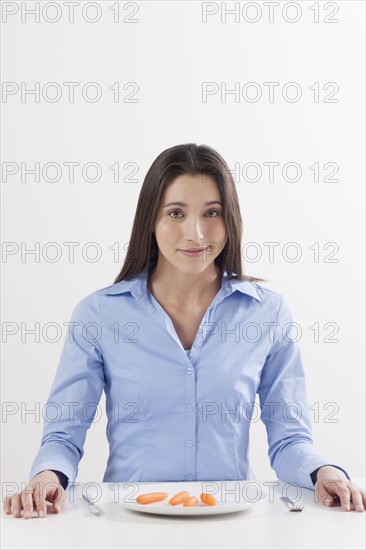 Studio shot of woman with baby carrots on plate. Photo : Jan Scherders