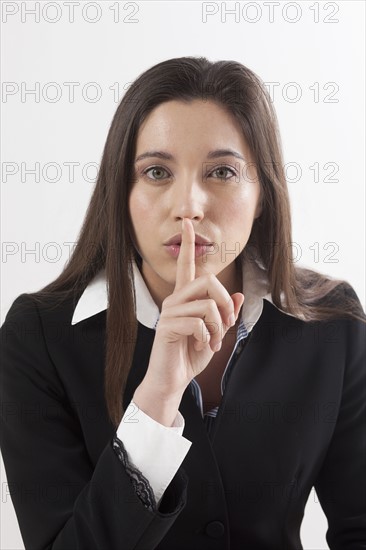 Young woman with finger on her lips, studio shot. Photo : Jan Scherders