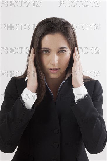 Portrait of young woman with hands covering ears, studio shot. Photo : Jan Scherders