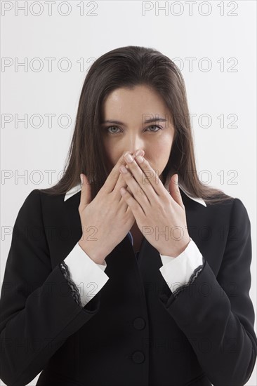 Portrait of young woman with hands covering lips, studio shot. Photo: Jan Scherders