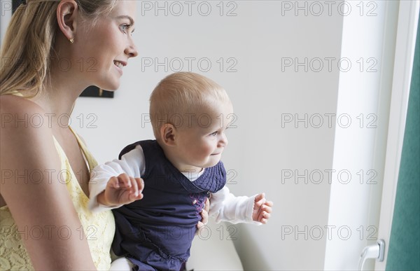 Young mother with daughter looking through window. Photo: Mark de Leeuw