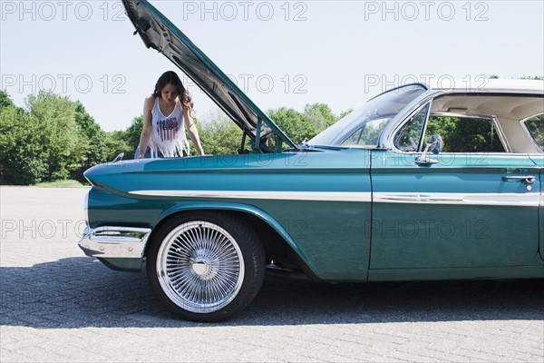 Woman standing near broken vintage car. Photo : Mark de Leeuw