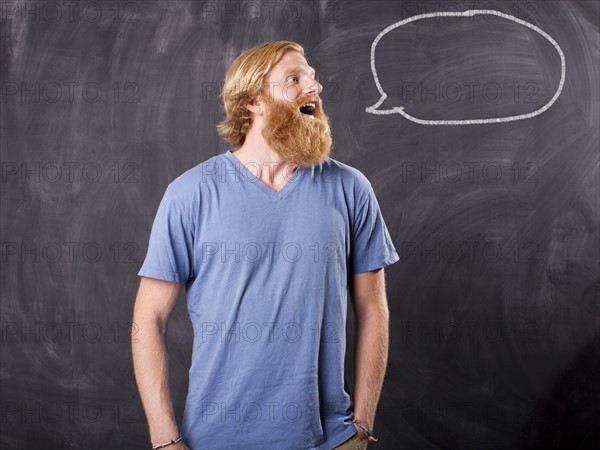 Man in front of blackboard with drawing depicting speech bubble. Photo : Jessica Peterson