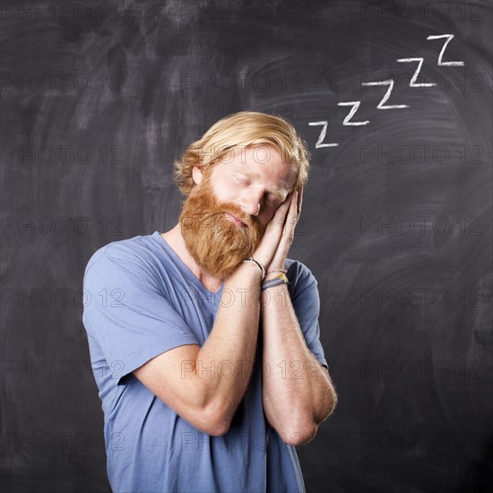 Man sleeping while standing in front of blackboard. Photo : Jessica Peterson