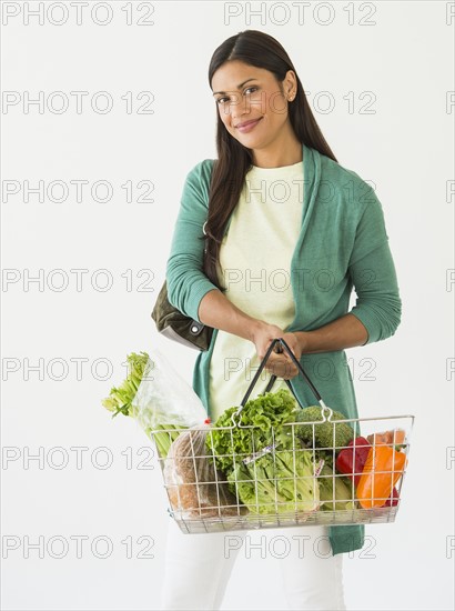 Studio shot of woman holding shopping basket with vegetables.