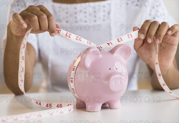 Woman measuring piggy bank.