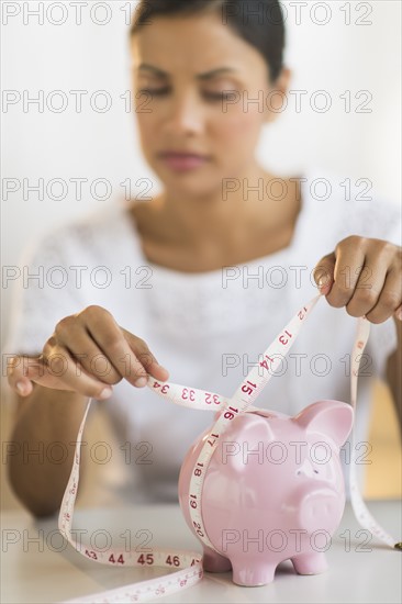 Woman measuring piggy bank.