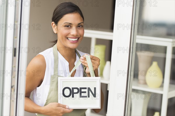 Woman standing in front of store and holding open sign.