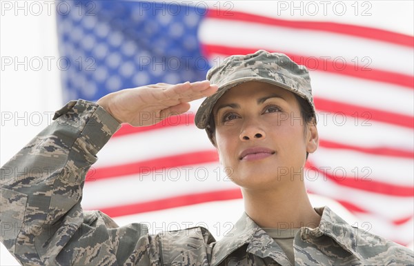 Female army soldier saluting, American flag in background.