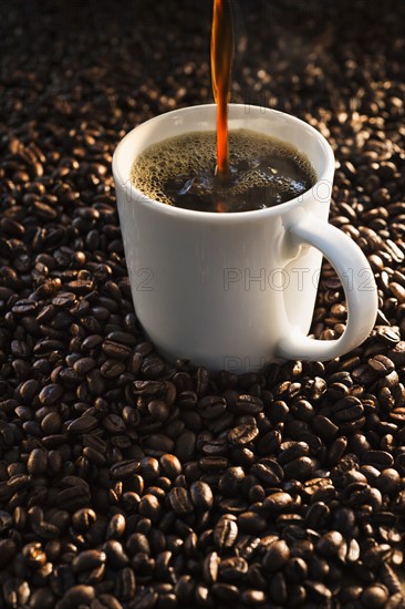 Pouring coffee into cup on coffee beans, studio shot.