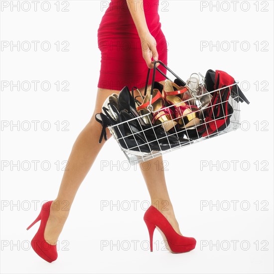 Low section of woman carrying shopping basket with shoes, studio shot.