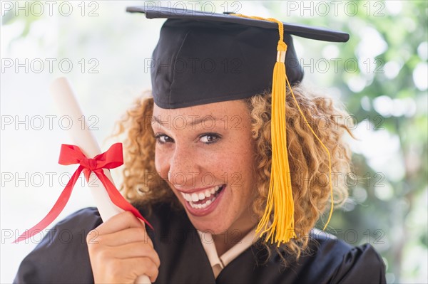 Portrait of smiling young woman in mortarboard showing diploma.